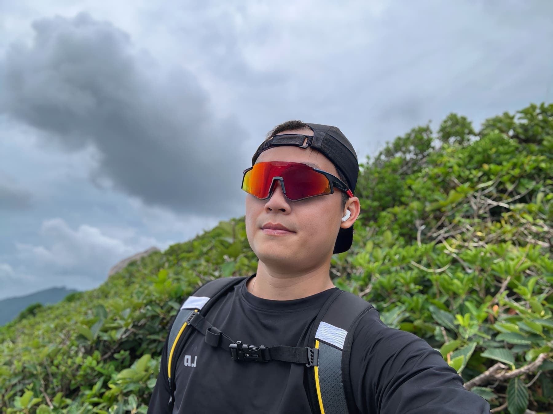 A hiker in red sport sunglasses and a backwards cap on a green hillside