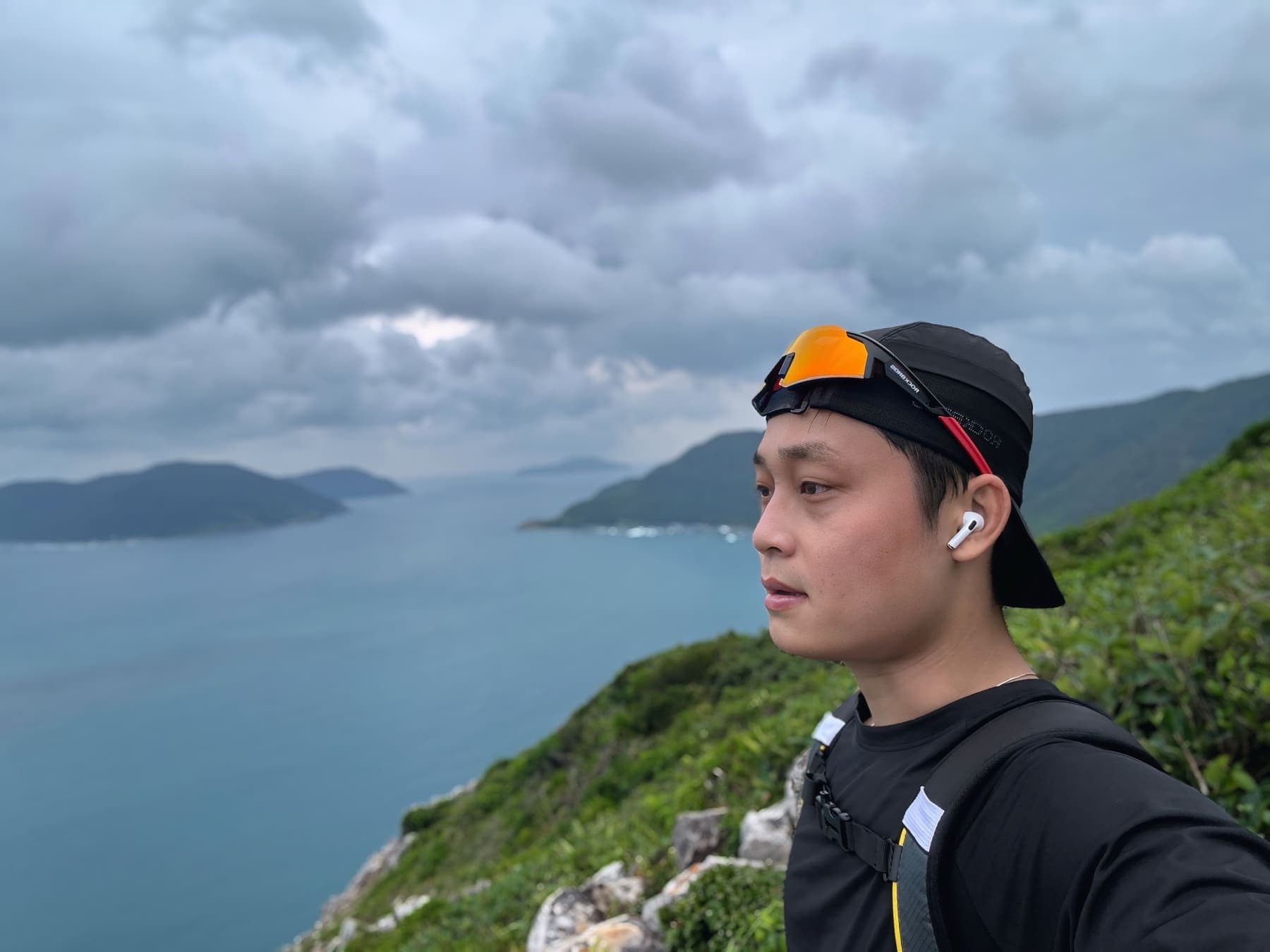 A hiker looking out over a bay and green islands under a cloudy sky