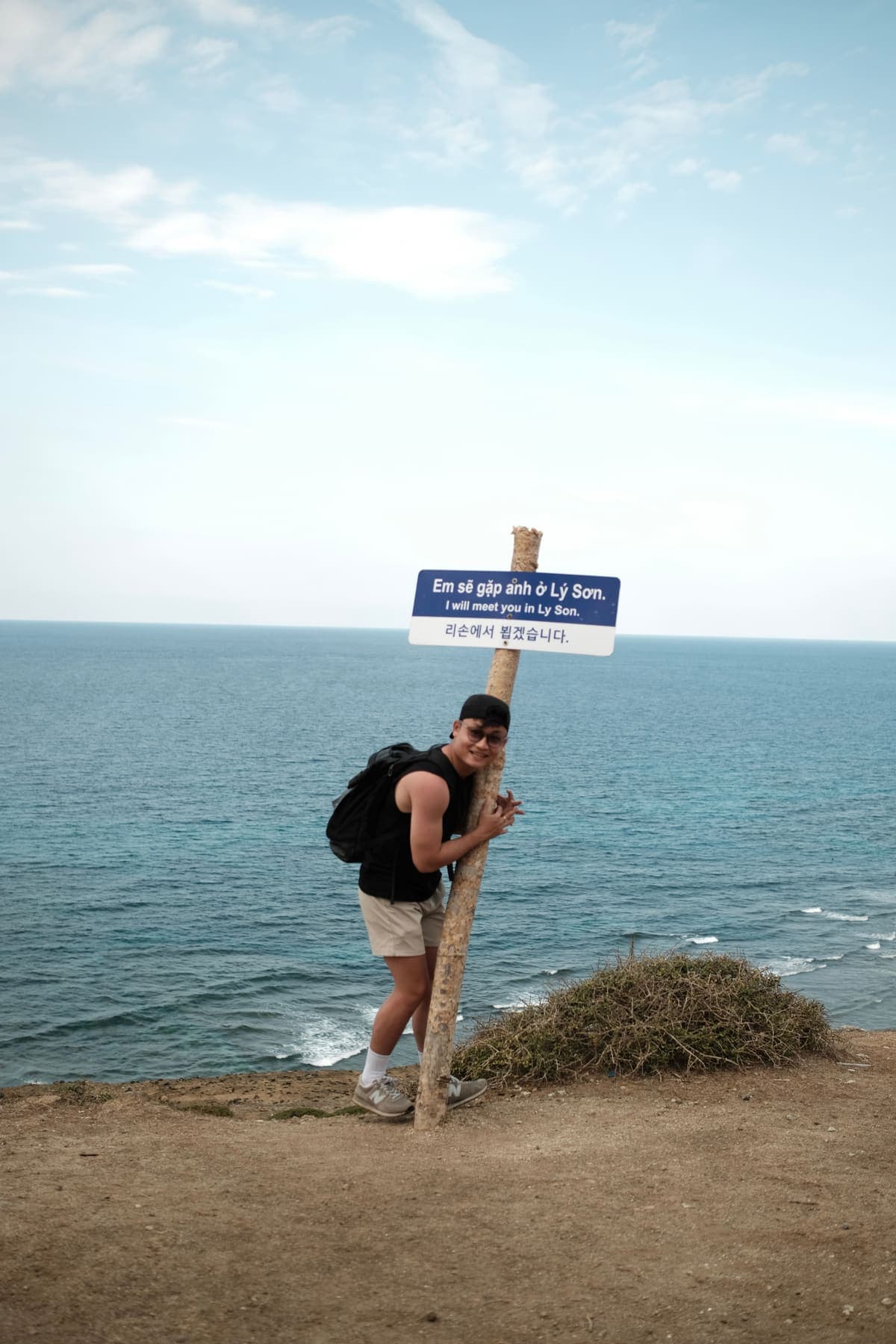 A man with a backpack holding a signpost on the clifftop above the sea
