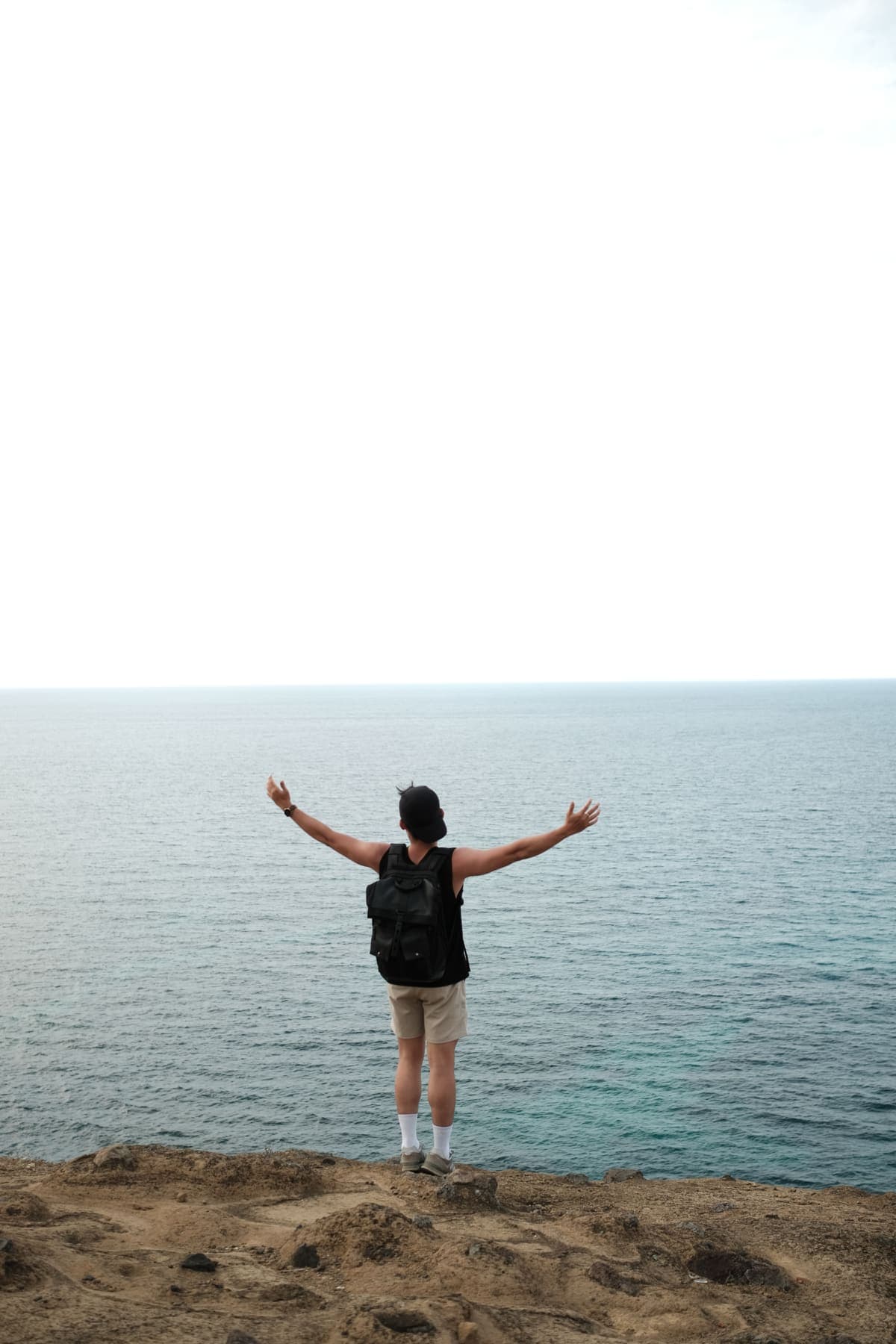 A man on the clifftop with his arms spread wide toward the sea