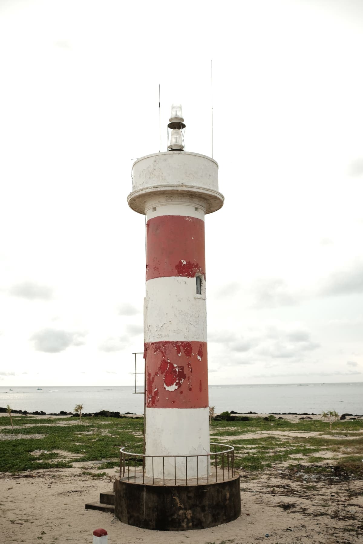 A red and white striped lighthouse on a grassy shore