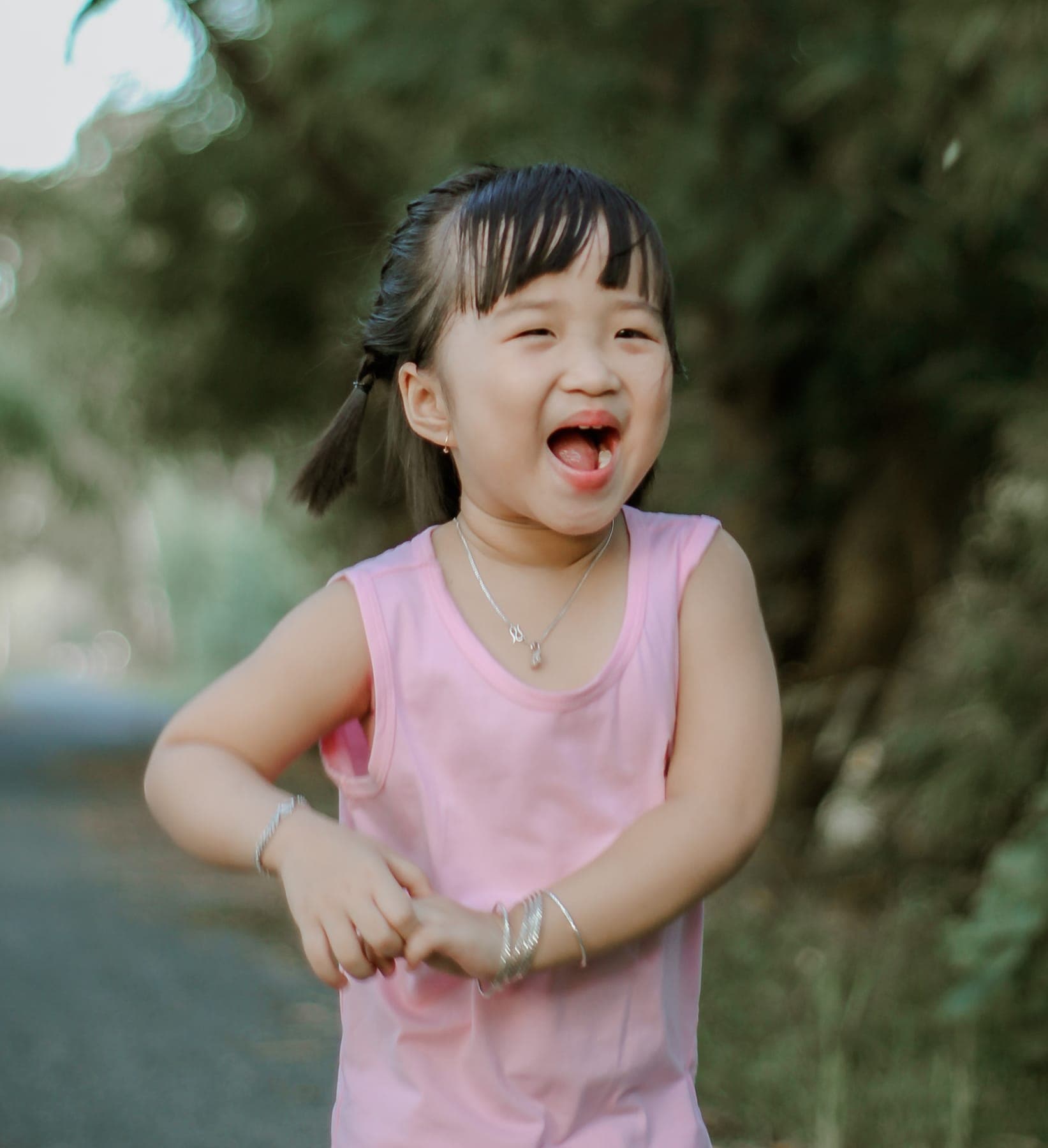 A little girl in a pink top laughing on a tree-lined path