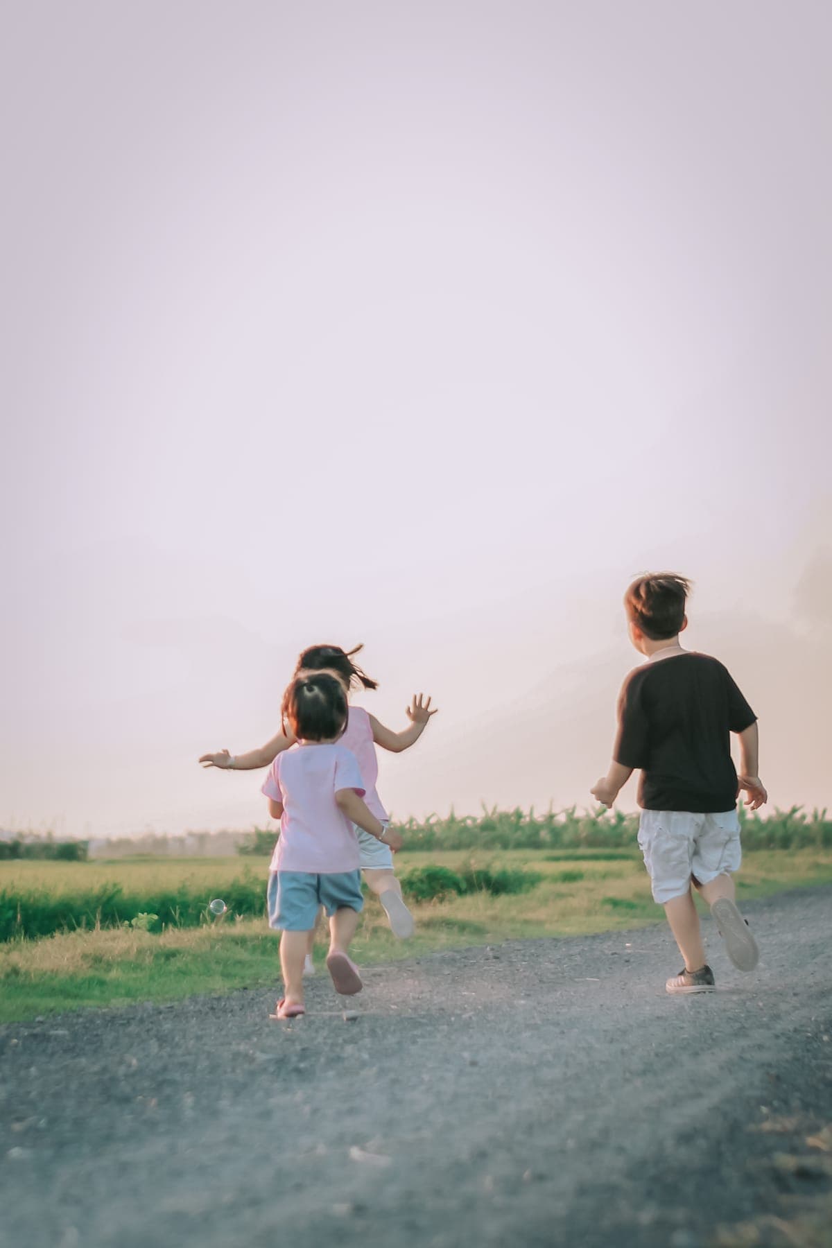 Three children running down a gravel road toward the horizon
