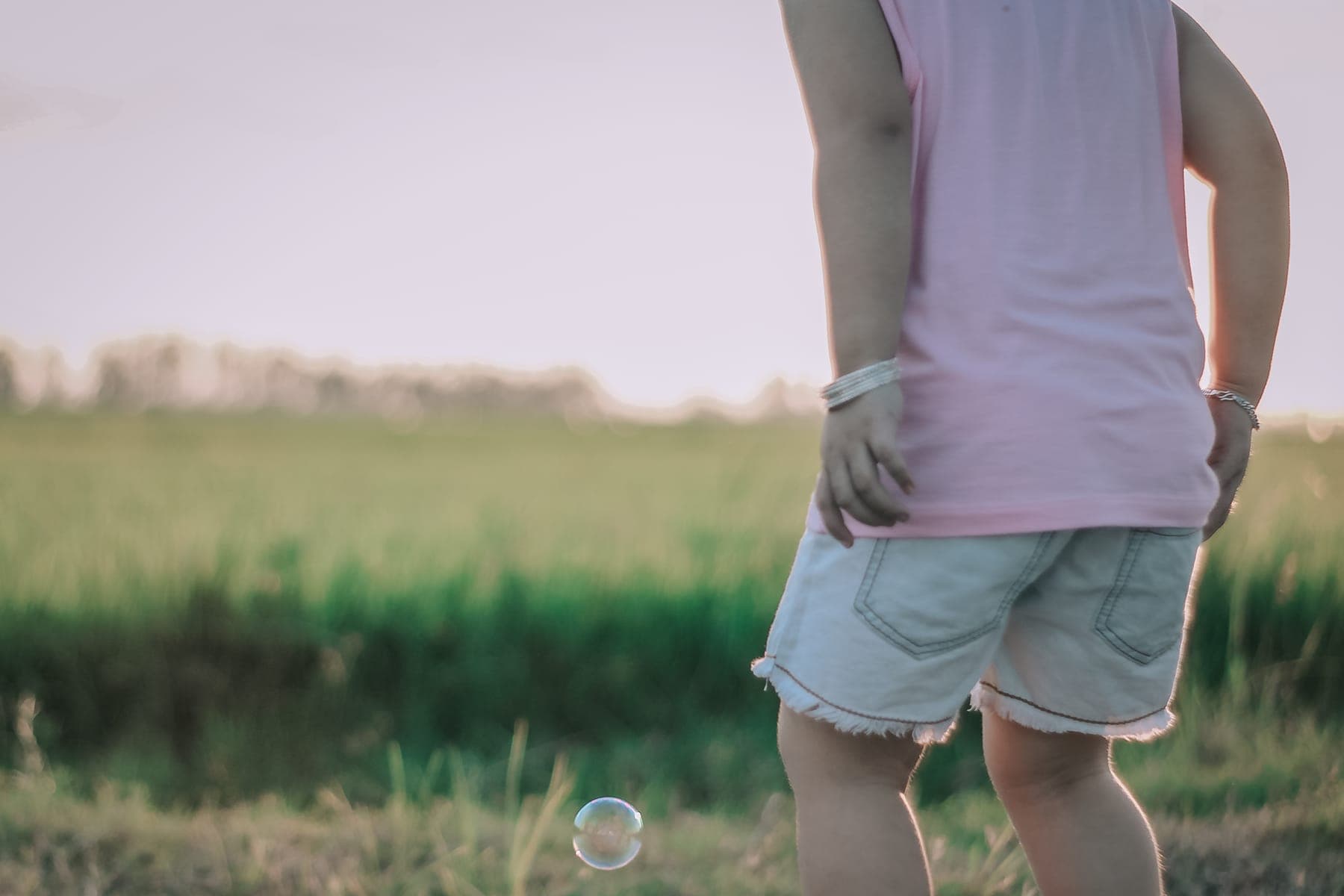 A child's legs and a soap bubble floating above the grass