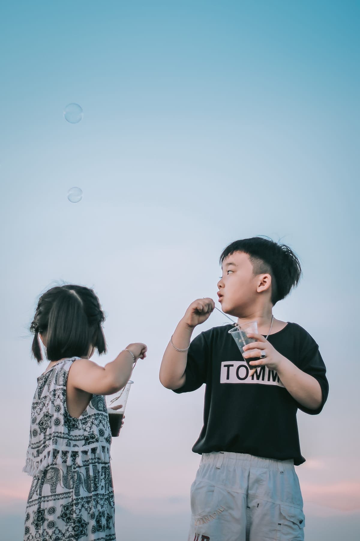 A boy and a girl blowing soap bubbles against a blue sky