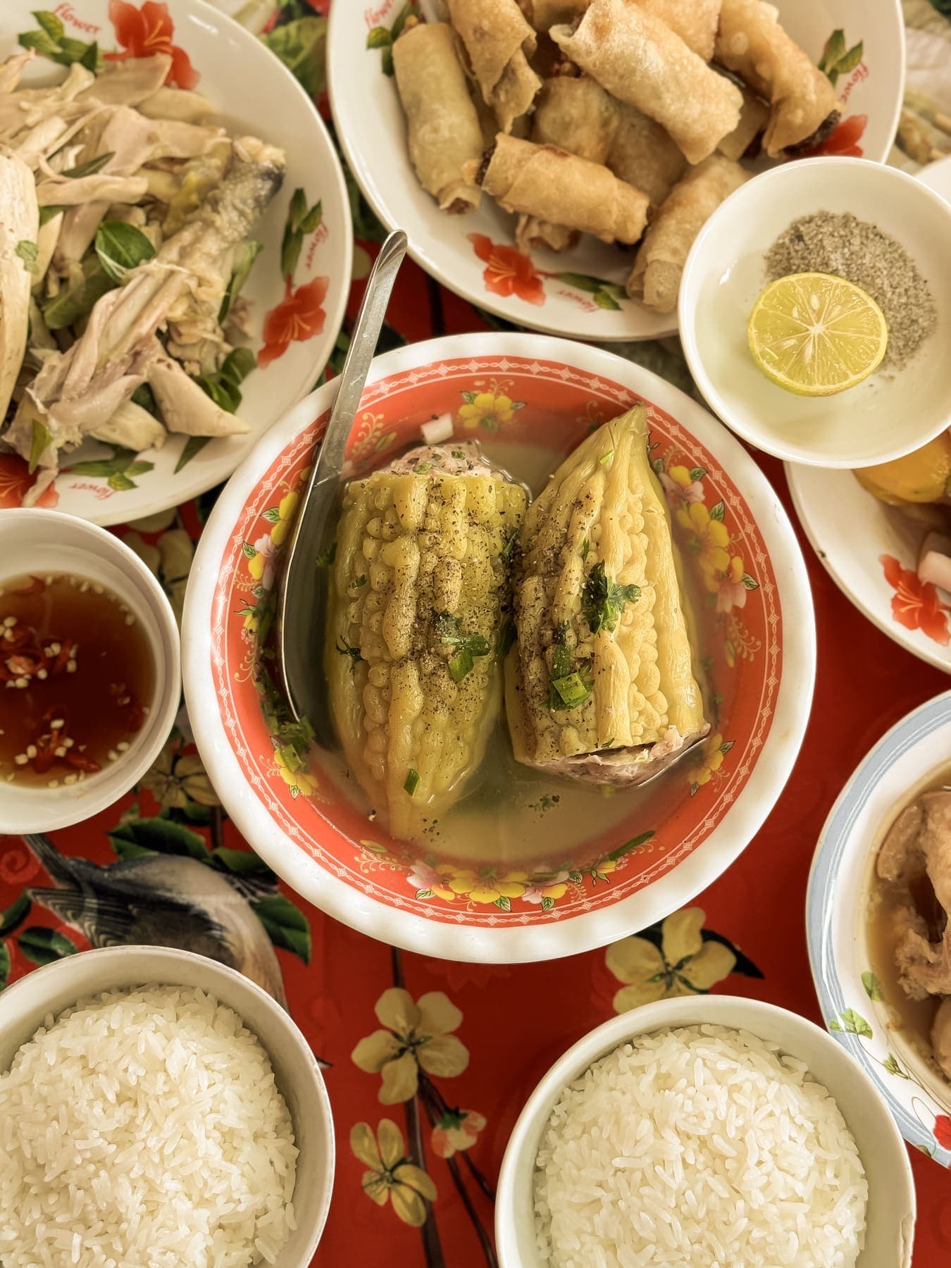 Stuffed bitter melon soup, spring rolls, shredded chicken and bowls of rice on a red cloth