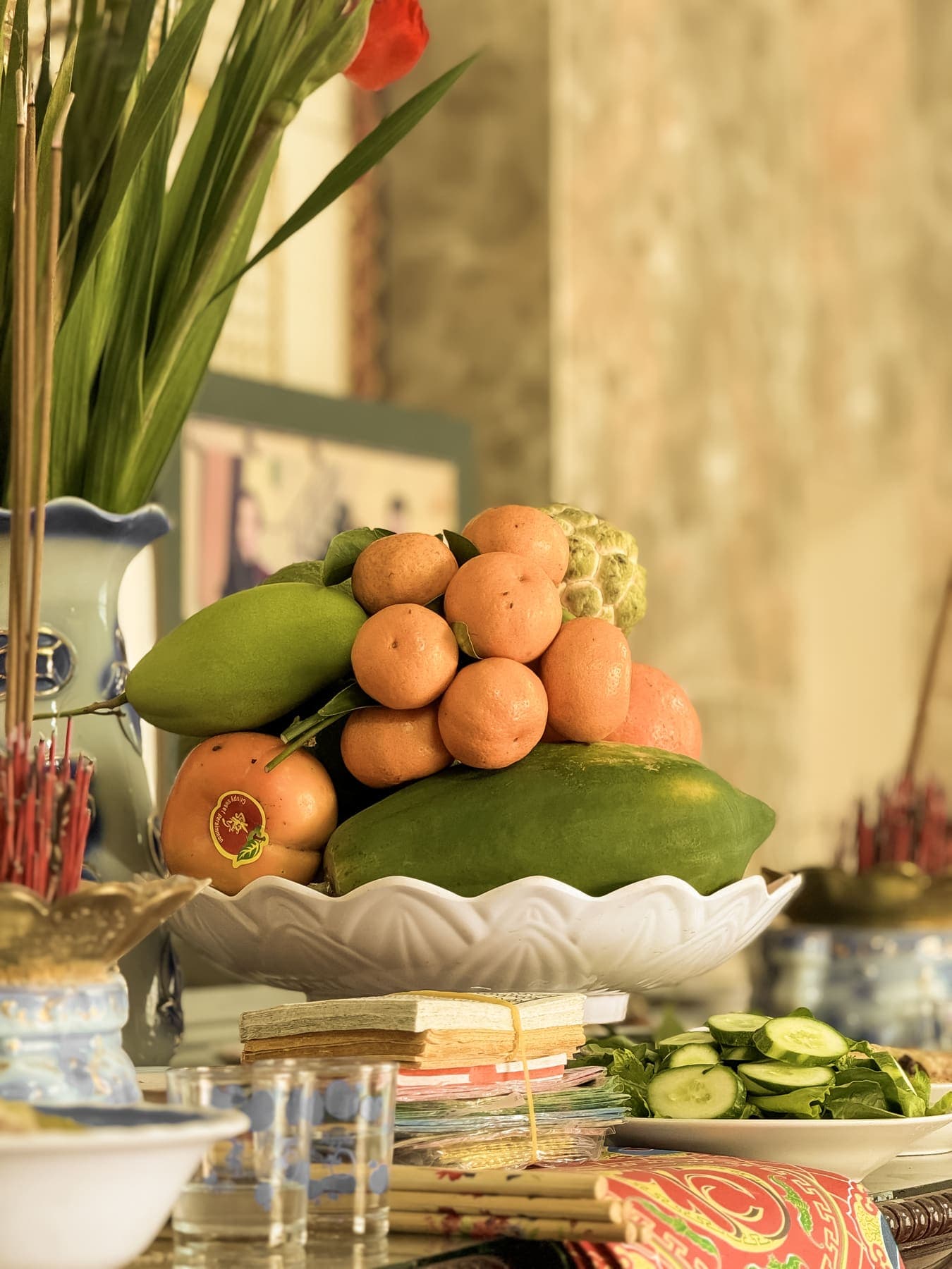 A tray of mandarins, mango and papaya on the altar beside a vase of leaves