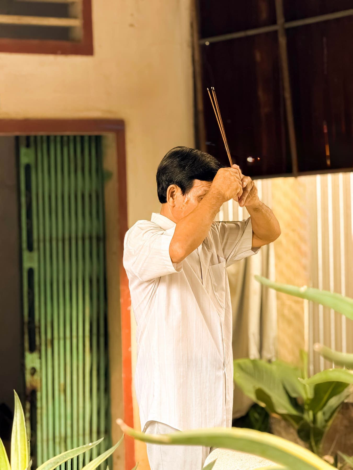 A man praying with incense beside a green-shuttered doorway