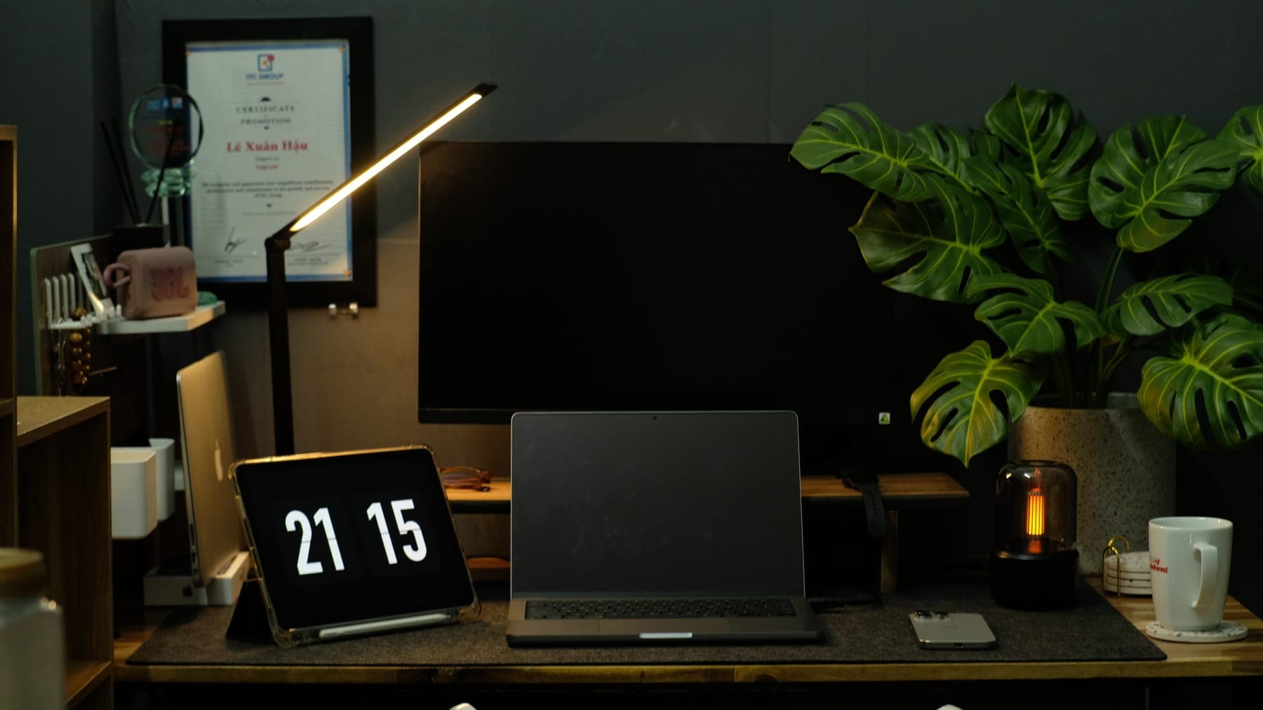 Desk lamp over a dark monitor, a flip clock at 21:15 and a lantern